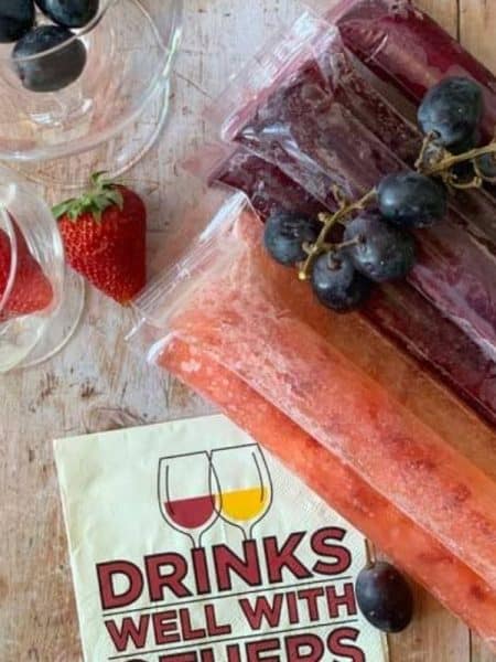 A wooden counter with pink and purple colored popsicles made of a wine mixture.
