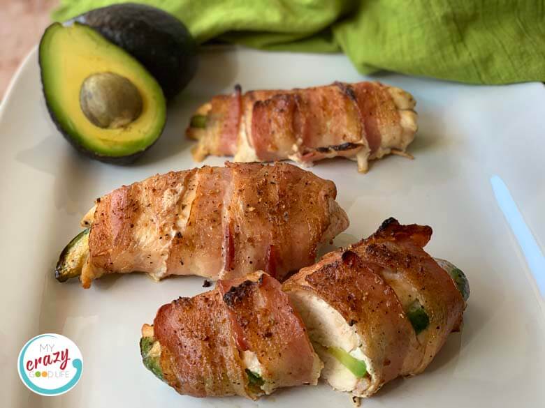 avocado stuffed bacon wrapped chicken on white platter with avocado in background