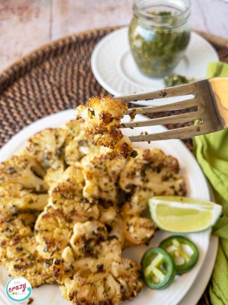 cauliflower steaks on a white plate with a fork full of food being lifted