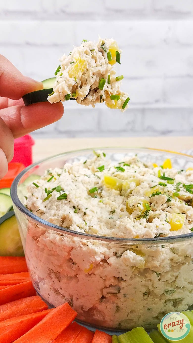 clear glass bowl of chicken salad with hand dipping cucumber