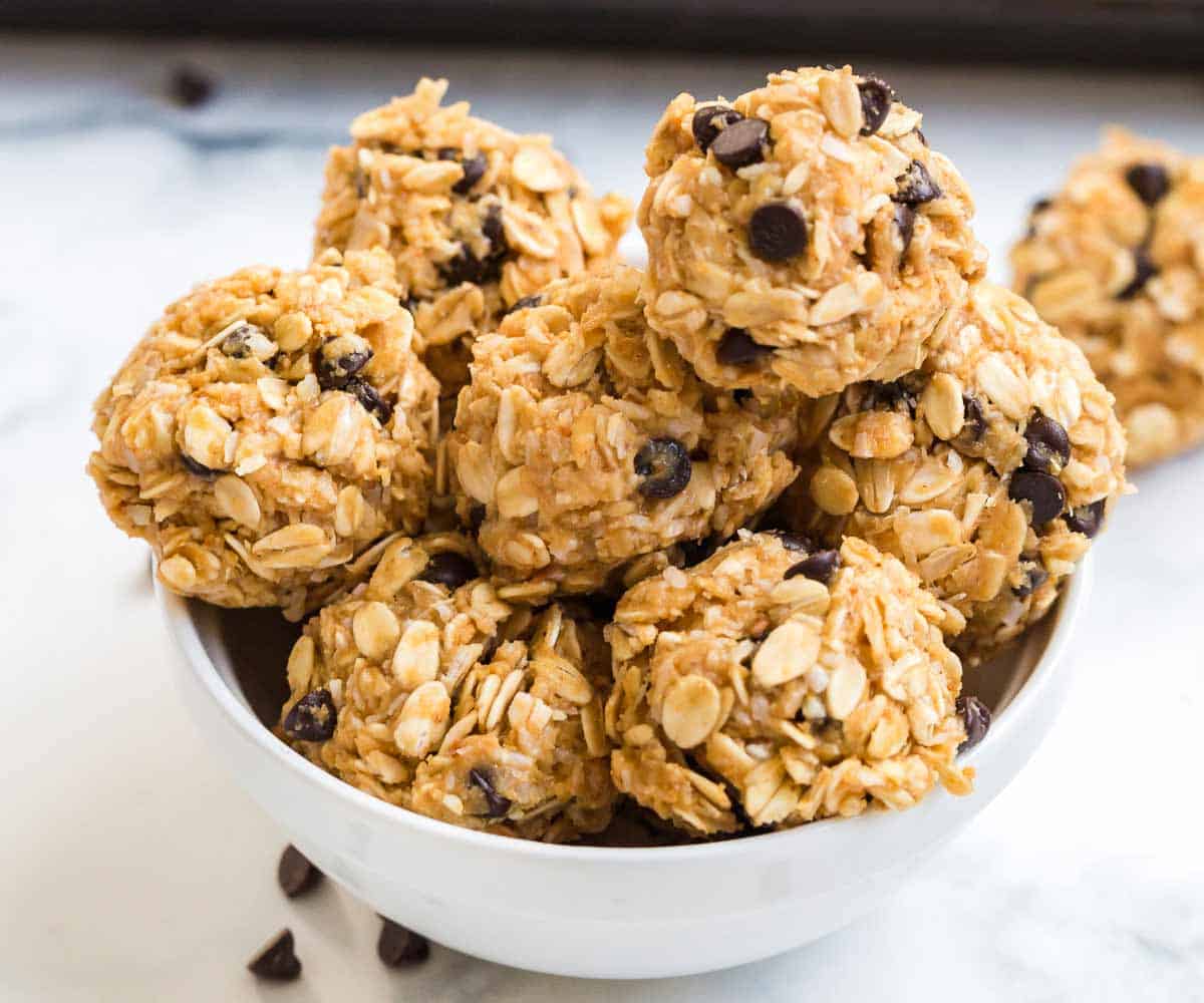 White bowl overflowing with peanut butter protein balls and chocolate chips. There is a white counter in the background. 