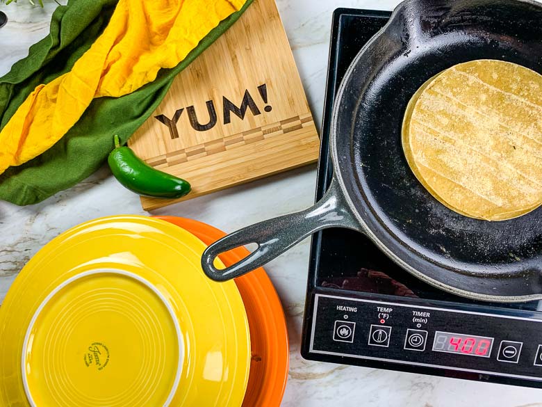 two plates with eggs and veggies in the middle, corn tortilla warming on pan