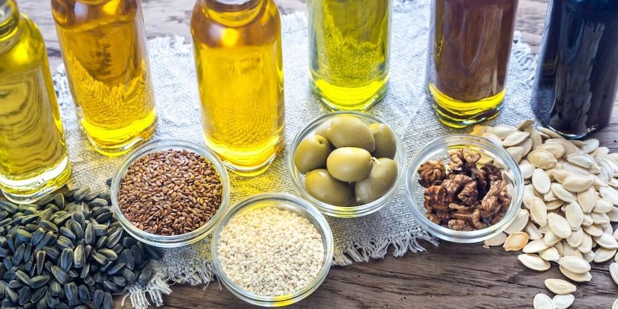 variety of oils in bottles in front of their main ingredients.