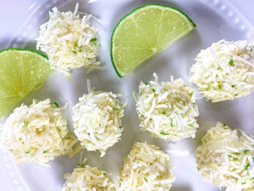 Image of lime coconut bites sitting on white plate. There are two lime wedges also on the plate.