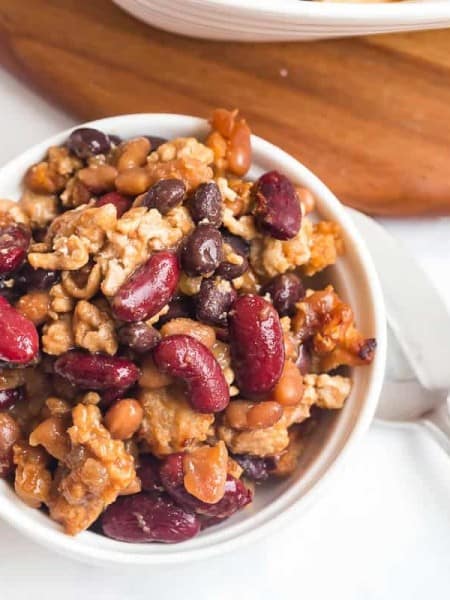 bowl of cooked baked beans on a white counter with a spoon and napkin underneath
