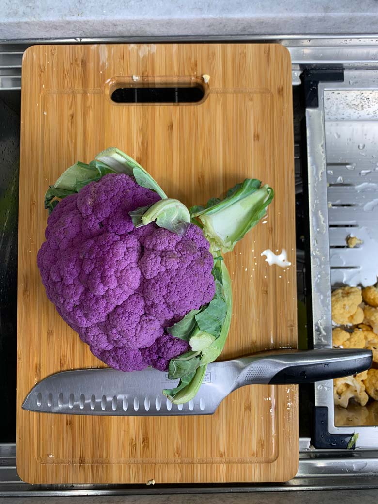 purple cauliflower and knife on wood cutting board