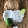 Coconut margarita in a clear glass next to opened coconut and lime.
