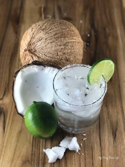 Coconut margarita in a clear glass next to opened coconut and lime.