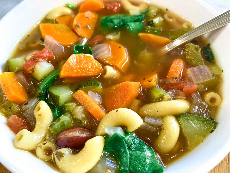 close up of minestrone soup in white bowl