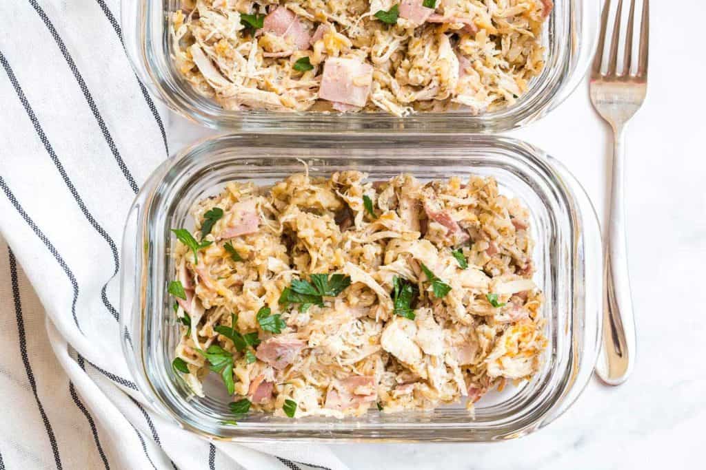 healthy crack chicken casserole in glass meal prep containers. White countertop in the background with a blue and white striped napkin to the left of the containers. 