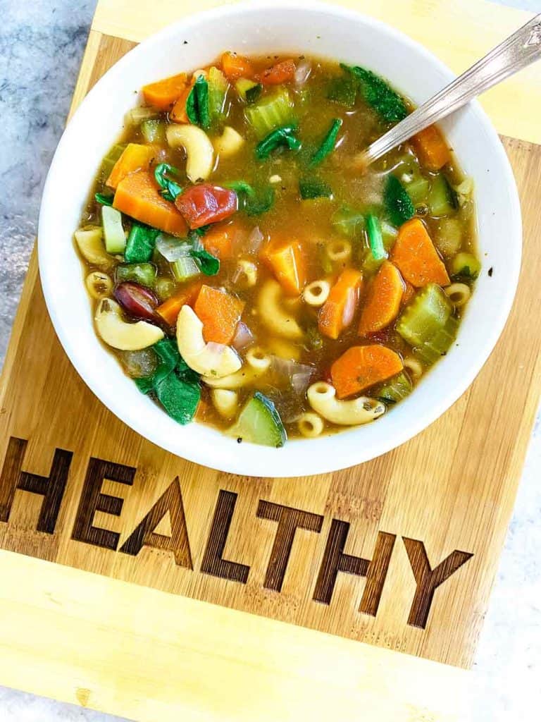 Vegan Minestrone Soup in white bowl on board that says Healthy