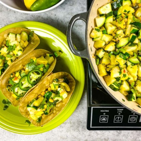 calabacitas and tacos on a green plate, garnished with jalapenos.