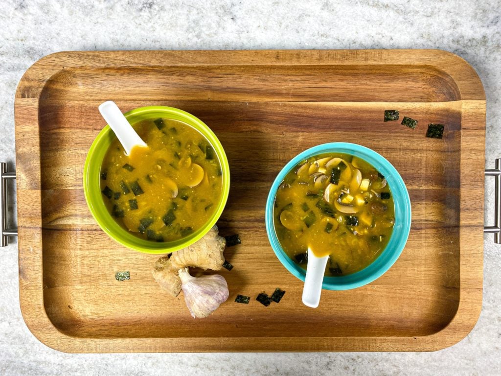 Blue and green bowl of miso soup on a cutting board