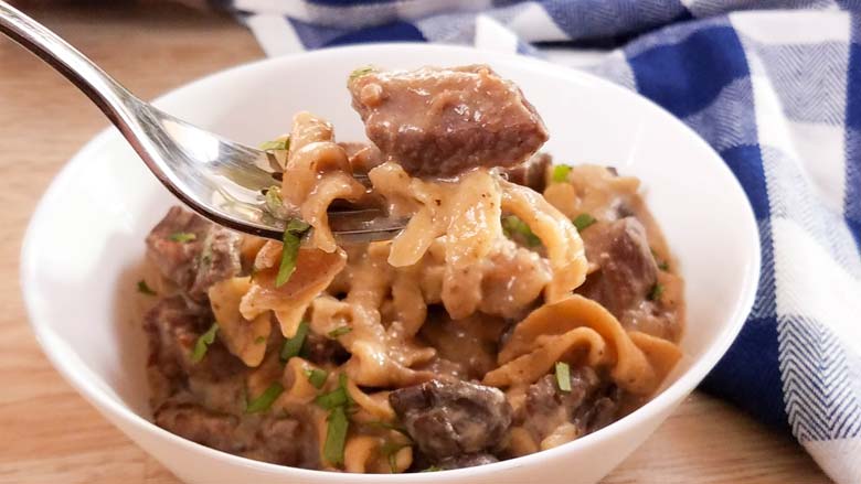 Beef stroganoff in a white bowl with a fork lifting a bite