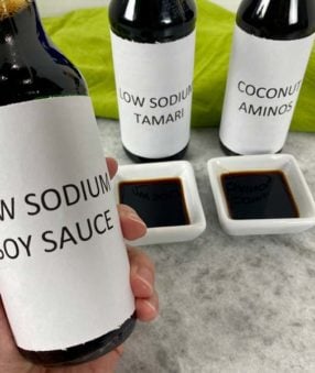 holding a bottle of low sodium soy sauce with aminos and tamari in the background