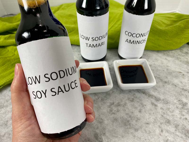 hand holding low sodium soy sauce, with tamari and coconut aminos in the background