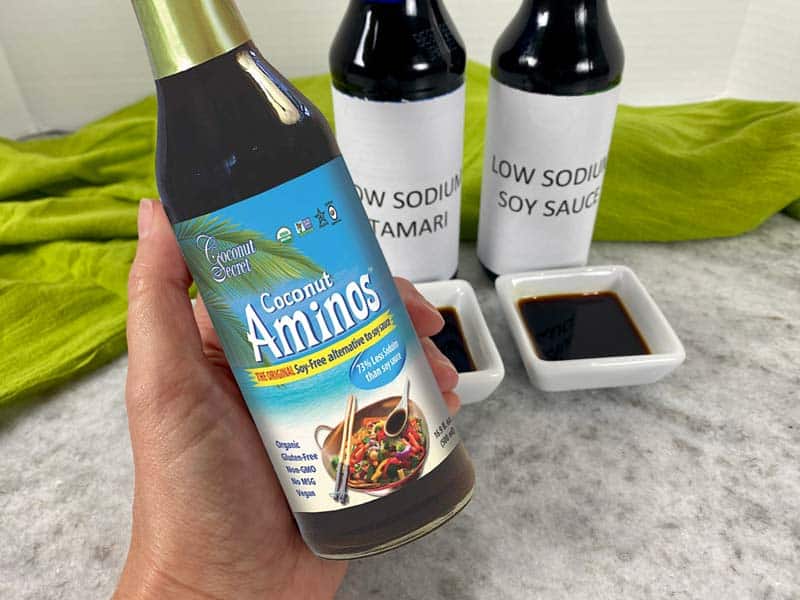 hand holding bottle of coconut aminos with green towel in background