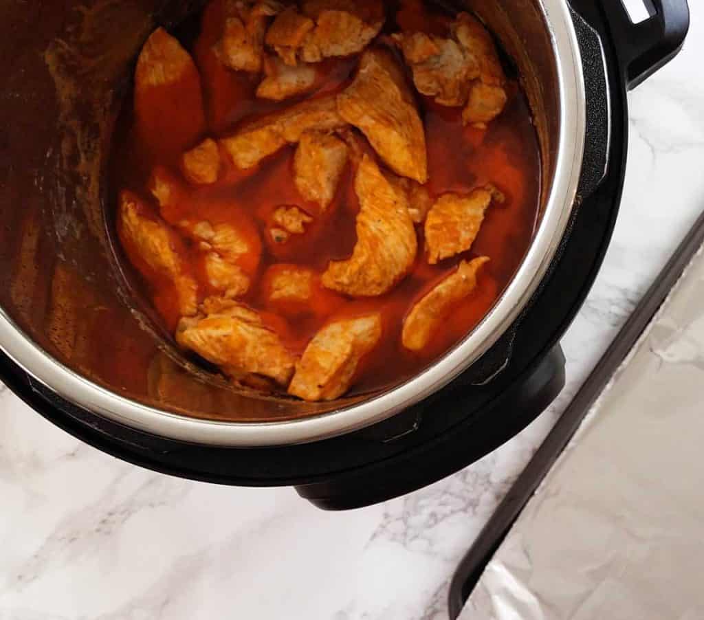 image from above of instant pot full of buffalo sauce and chicken pieces