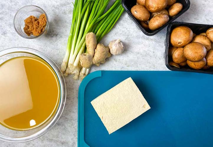 block of tofu on a blue cutting board with ingredients for miso soup