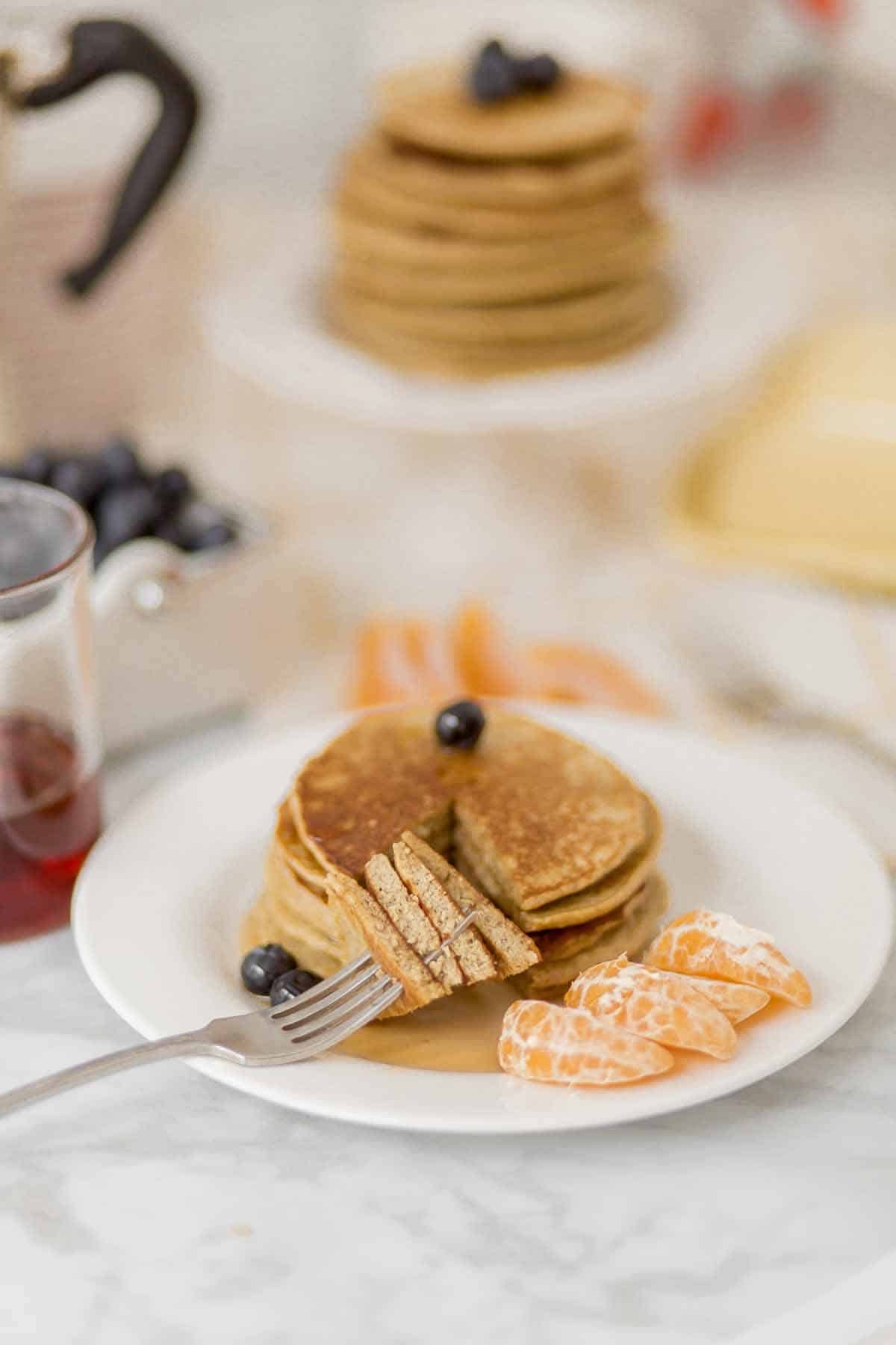 Stack of pancakes on a white plate. A bite of the pancakes are cut and speared onto a fork, which is lying on the pate.