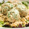 close up of cooked swedish meatballs on a white plate on top of lettuce and rice