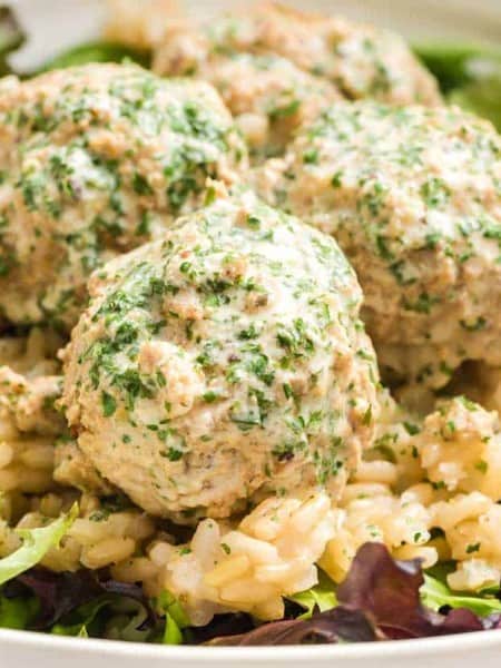 close up of cooked swedish meatballs on a white plate on top of lettuce and rice.