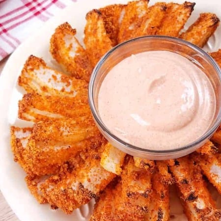 A white bowl with a cut and air fried blooming onion and in the center is a glass bowl of spicy dipping sauce.