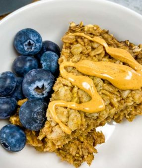bowl of amish baked oatmeal with blueberries on the side and peanut butter on top