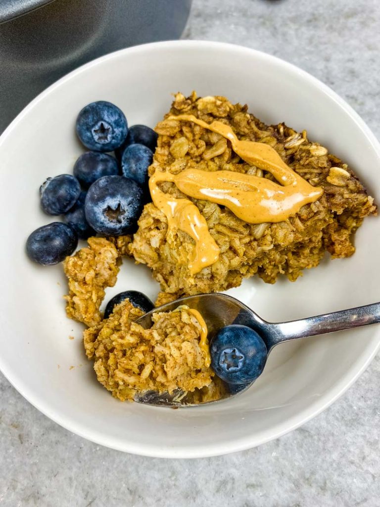 baked oatmeal on a spoon with a white bowl of oatmeal below