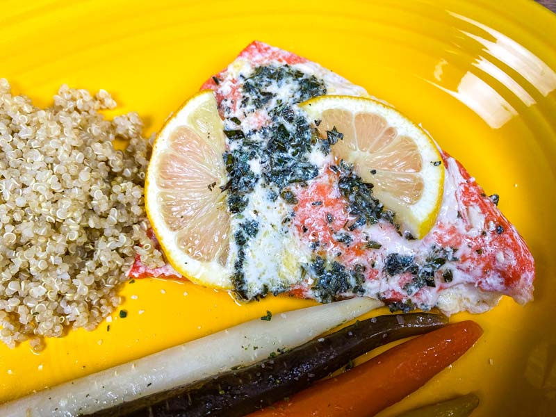 cooked salmon on a yellow plate with carrots and quinoa