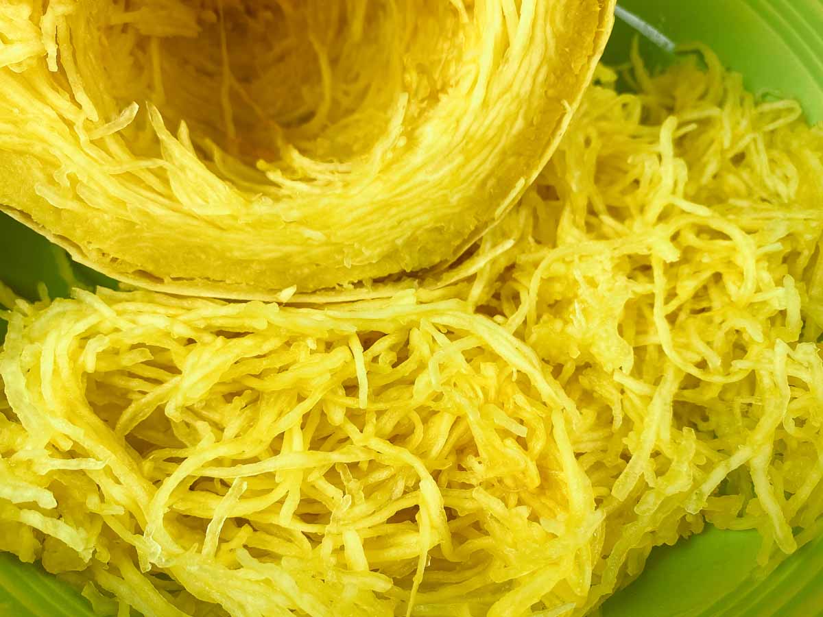 Half of cooked spaghetti squash next to a pile of cooked spaghetti squash on a green plate. 