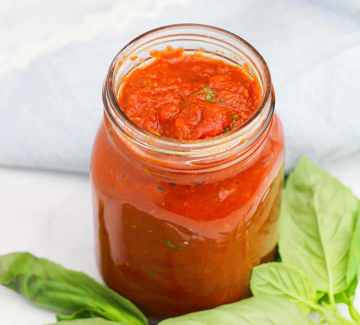 Mason jar of homemade spaghetti sauce with fresh basil on the counter underneath.