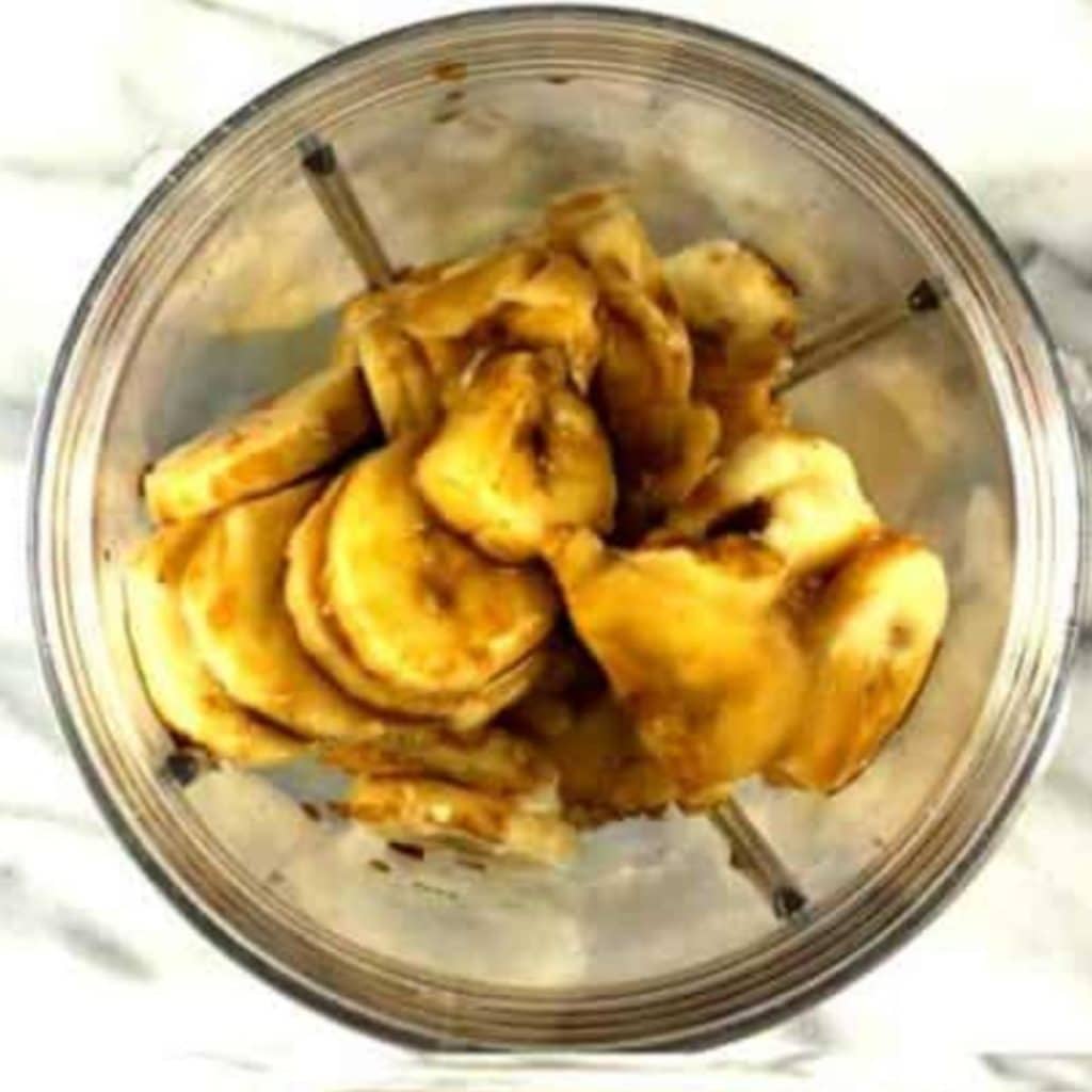 A blender with sliced bananas, almond milk, cocoa powder, and vanilla extract.