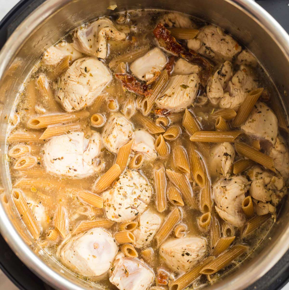 chicken and pasta being cooked in broth inside an instant pot.