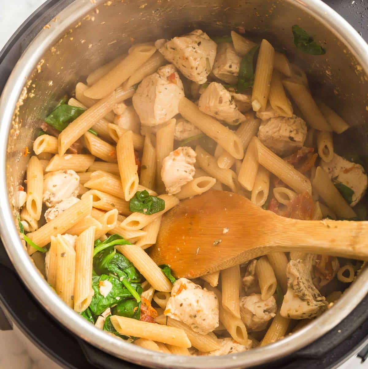 liquid cooking pasta, chicken and spinach inside an instant pot.