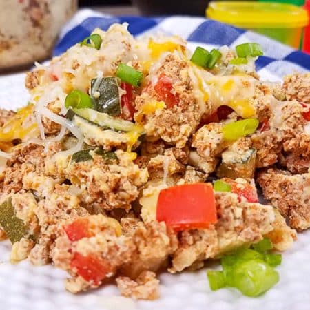 White plate with turkey chorizo and a fork. You can see red and green vegetables in the chorizo, with cheese on top.