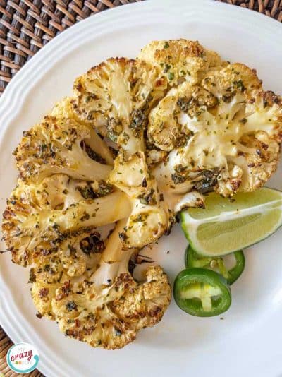 Cauliflower steak on white plate. Garnishes of jalapeno and lime are also on plate.