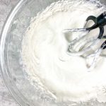 top down view of coconut whipped cream in glass bowl with beaters
