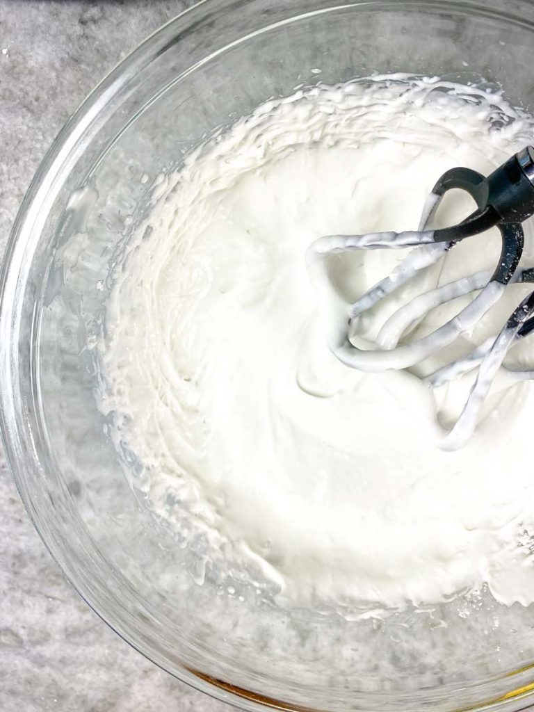 top down view of coconut whipped cream in glass bowl with beaters