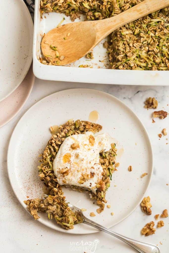 baked oatmeal in a white dish with piece cut out, on pwhite playe with greek yogurt and agave