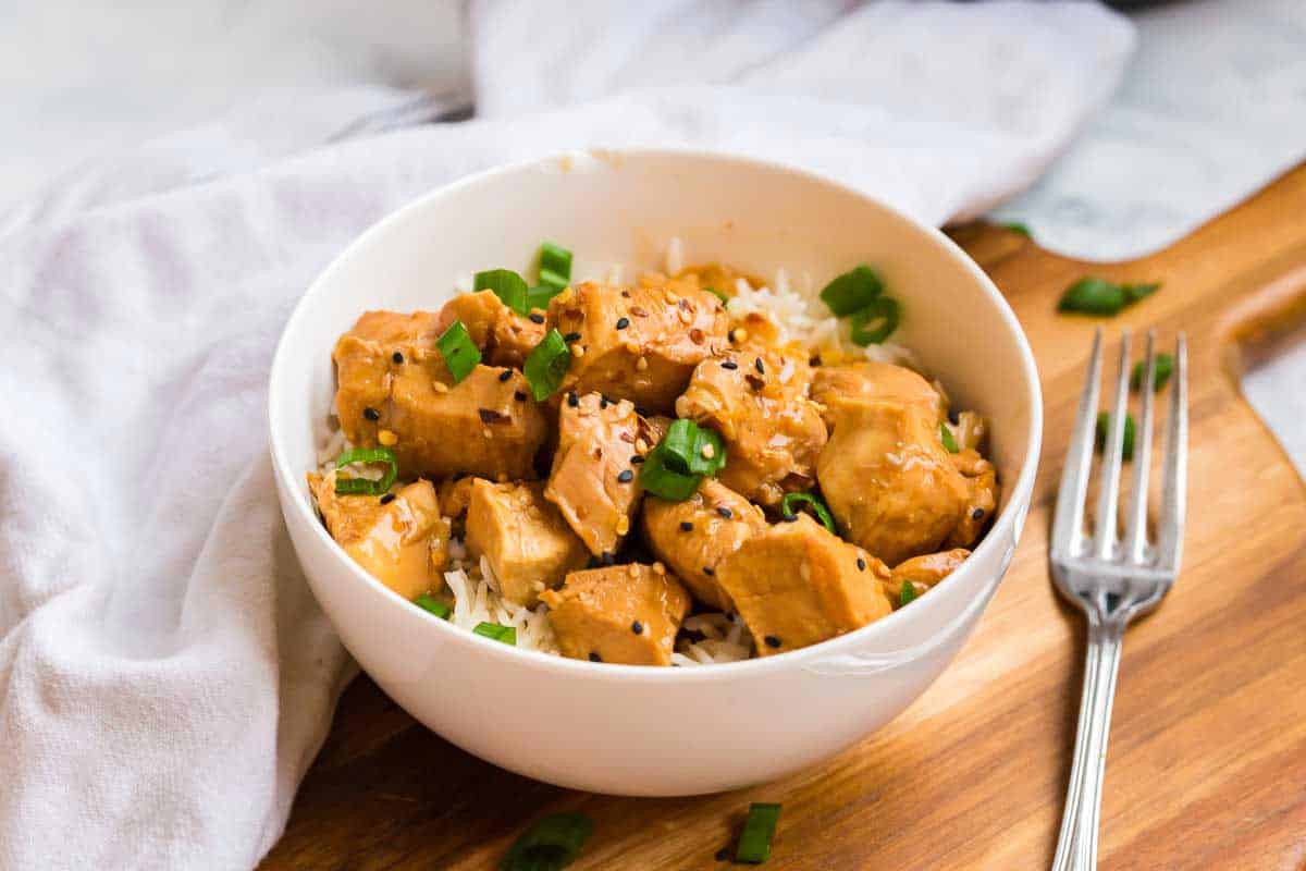 A white bowl with rice and a healthy orange chicken topped with green onions.