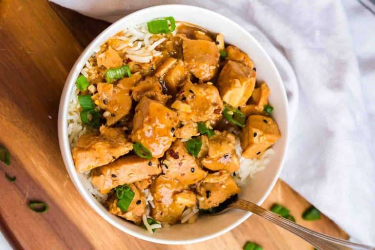 A white bowl with rice and a healthy orange chicken topped with green onions.