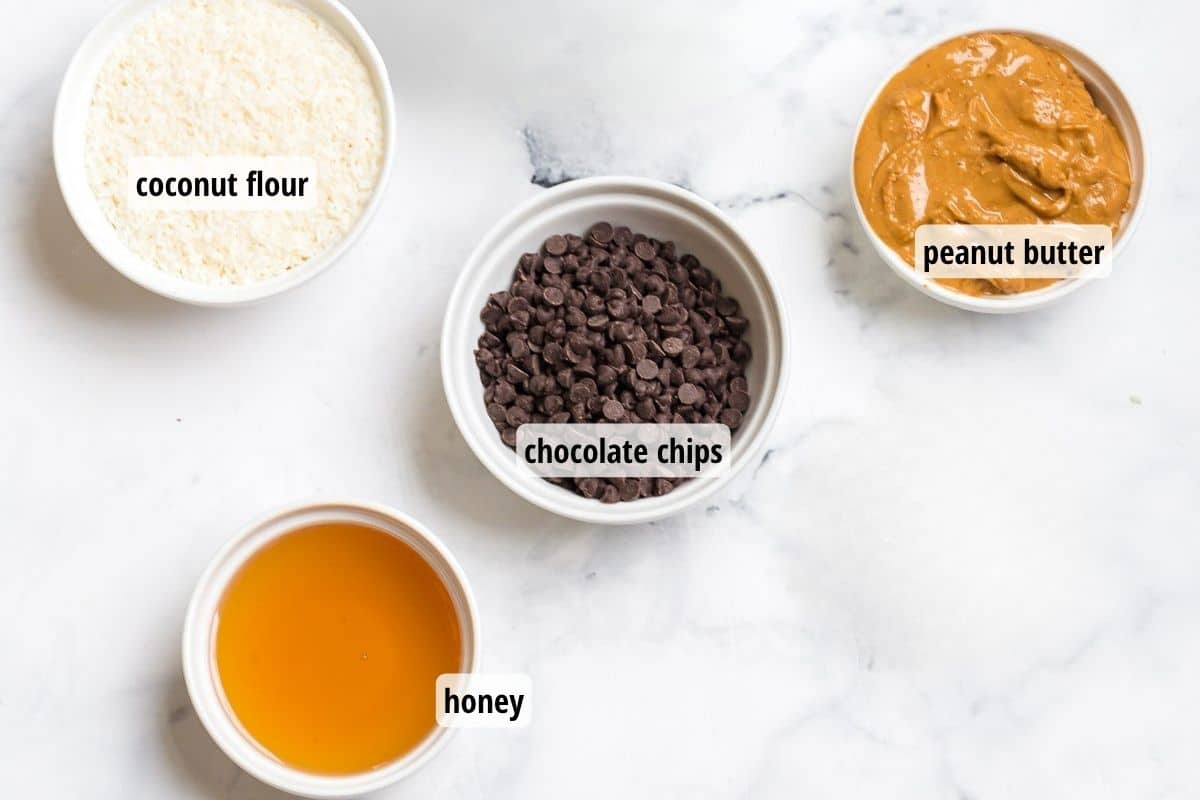 A white marbled counter top with four bowls of labeled ingredients to make healthy buckeyes.