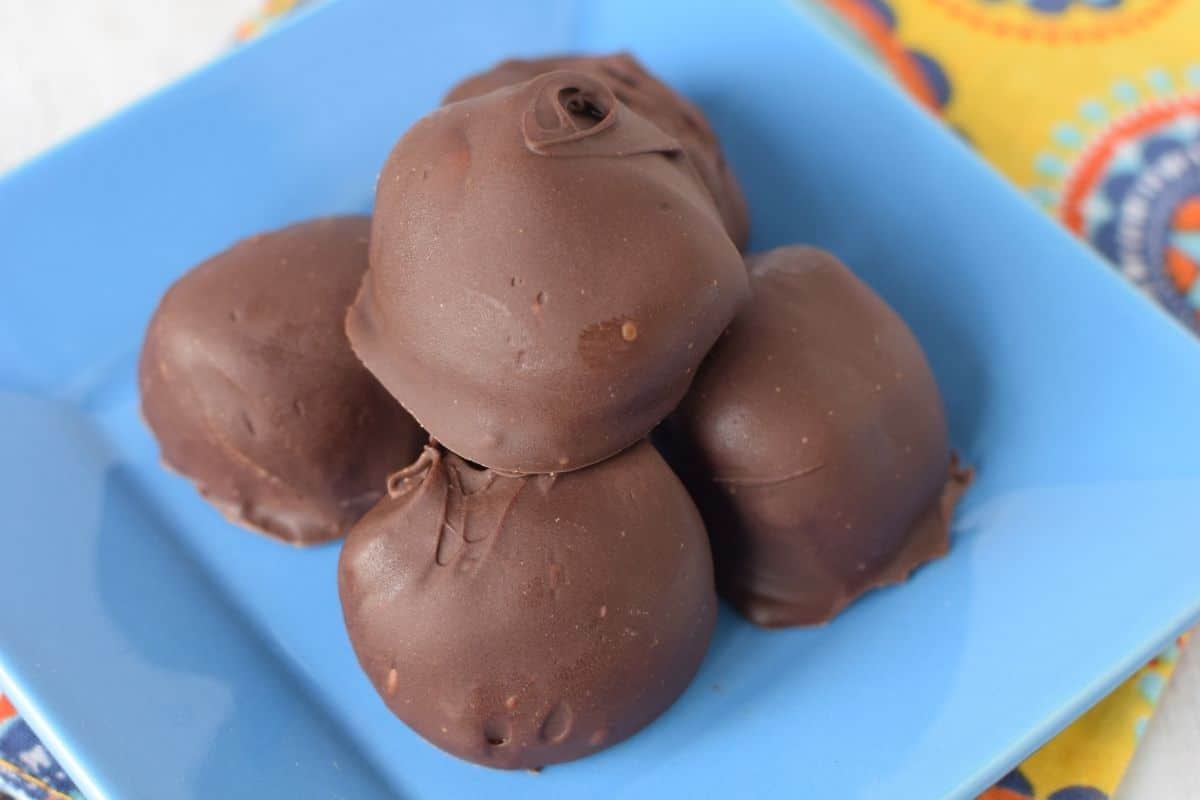 A blue square plate with 5 chocolate peanut butter buckeyes stacked together.