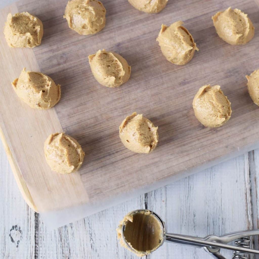 A wooden cutting board topped with parchment that has balls of sweet and creamy peanut butter balls on top.