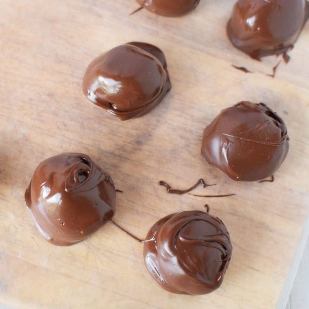 A wood cutting board with 6 freshly dipped buckeyes in melted chocolate.