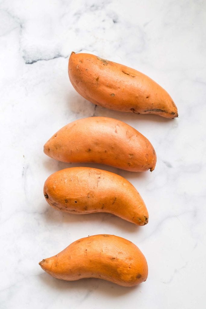 four raw sweet potatoes on a white marble countertop