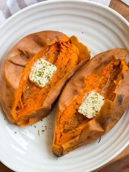 two cooked whole sweet potatoes, cut in half and dressed with butter and dried parsley.