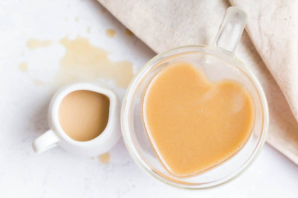 heart shaped mug of coffee with small creamer on white counter