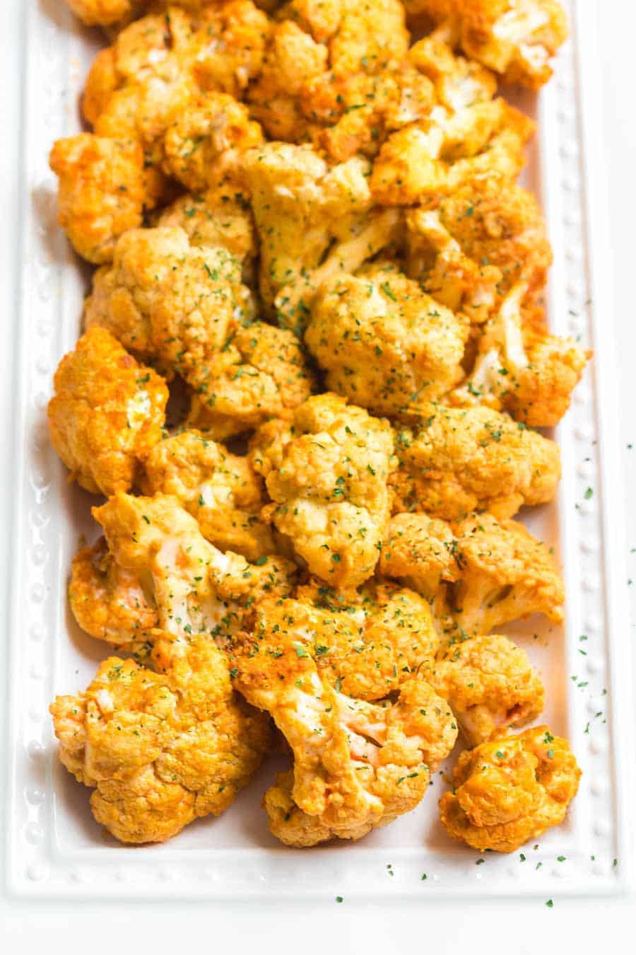 Cooked buffalo cauliflower on a white platter. You can see the ranch seasonings on the cauliflower. 